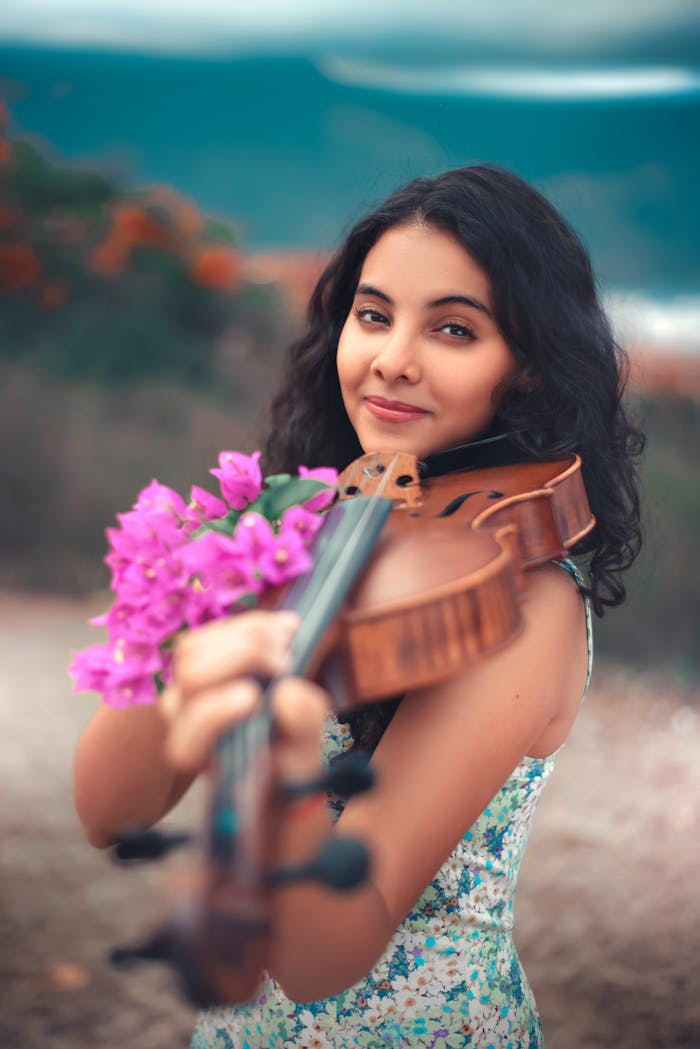De Manila a Barcelona: Un Viaje Musical por los Países del Concurso Smiling young woman holding a violin with pink flowers, outdoors in a vibrant setting.