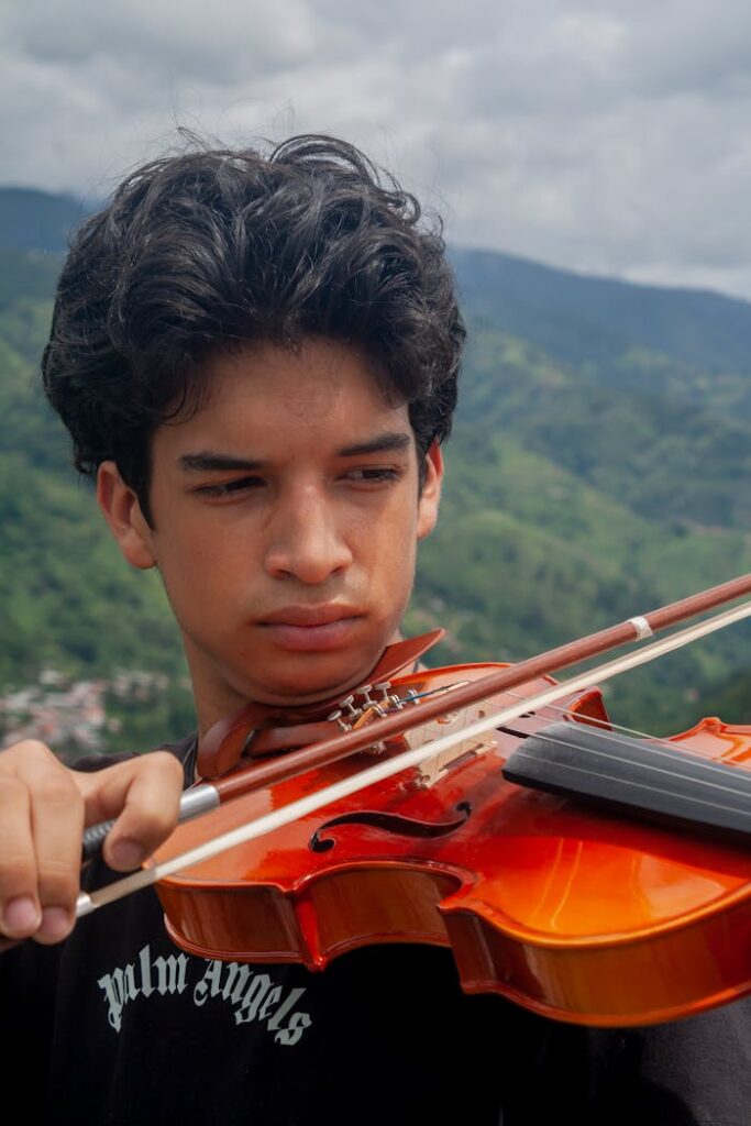 Teenage musician plays violin outdoors with a Venezuelan mountain backdrop, showcasing concentration and skill.